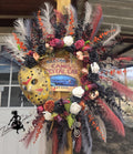 Decorative wreath with feathers and flowers in front of a 'Welcome to Camp Crystal Lake' sign.