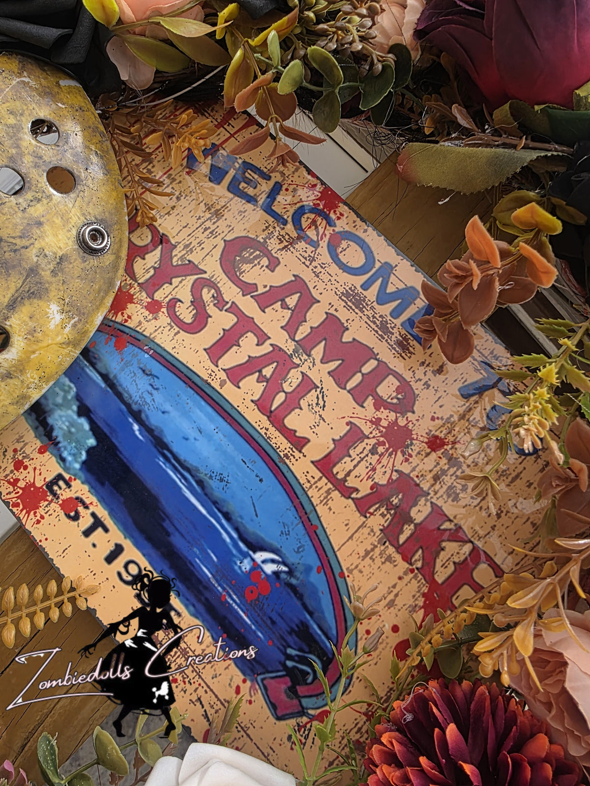 Decorative sign with 'Welcome to Camp Crystal Lake' text, surrounded by foliage and a shell.
