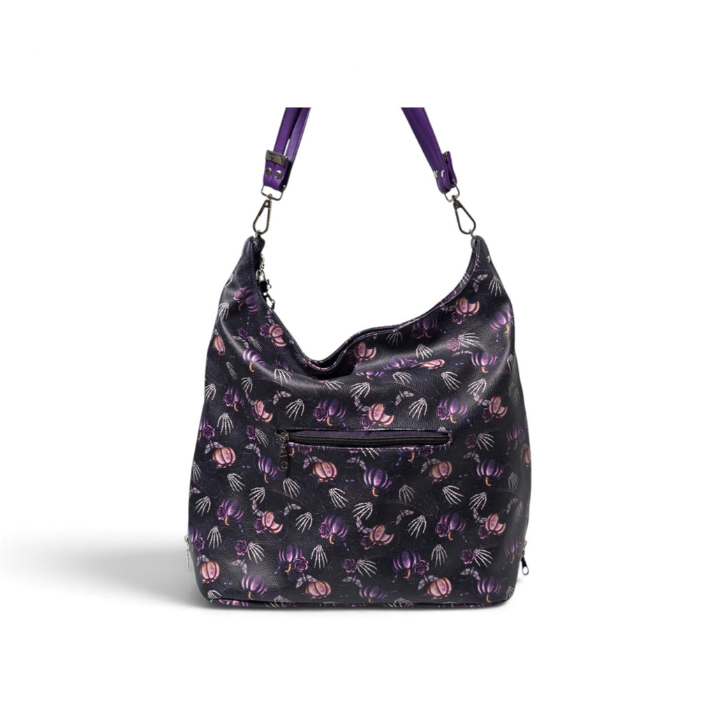 A black hobo-style shoulder bag with a purple and pink floral pattern, featuring a front zippered pocket and purple shoulder straps, shown against a plain white background.