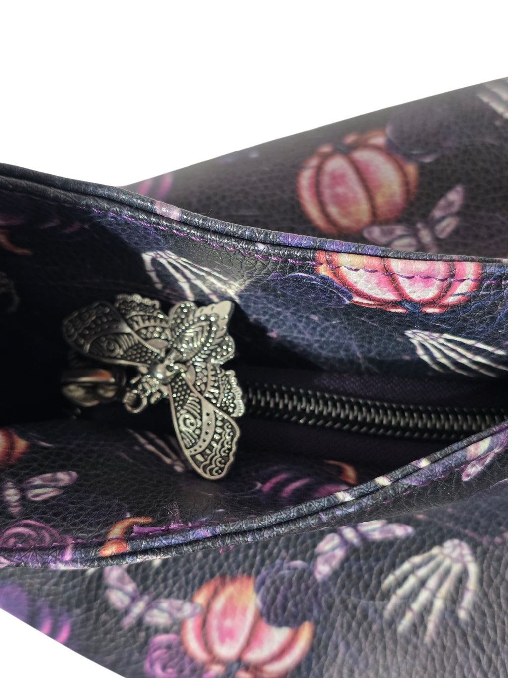 Close-up of a dark floral-patterned bag interior with a silver metal zipper and ornate silver zipper pull featuring a moth design.