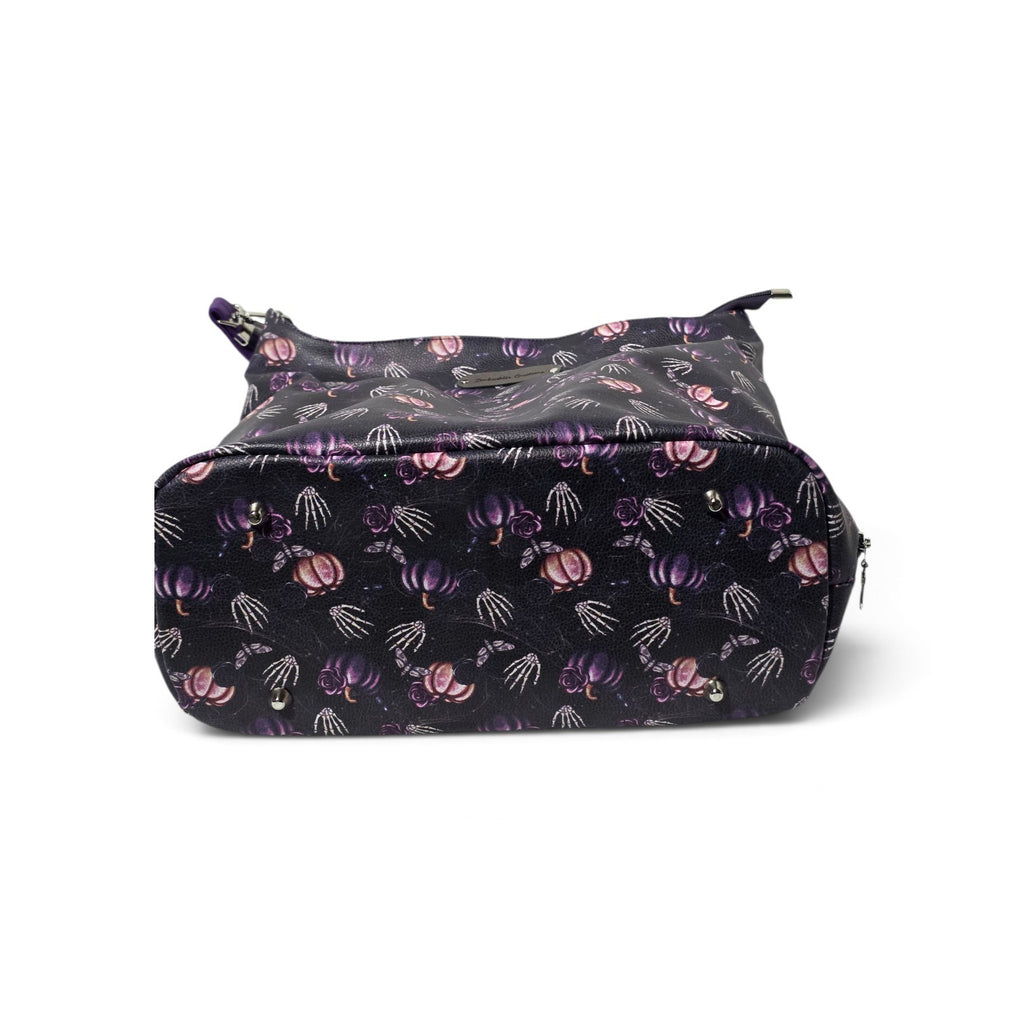 A black zippered hobo bag featuring a repeating pattern of purple pumpkins, pink pumpkins, and white skeleton hands, shown against a plain white background.