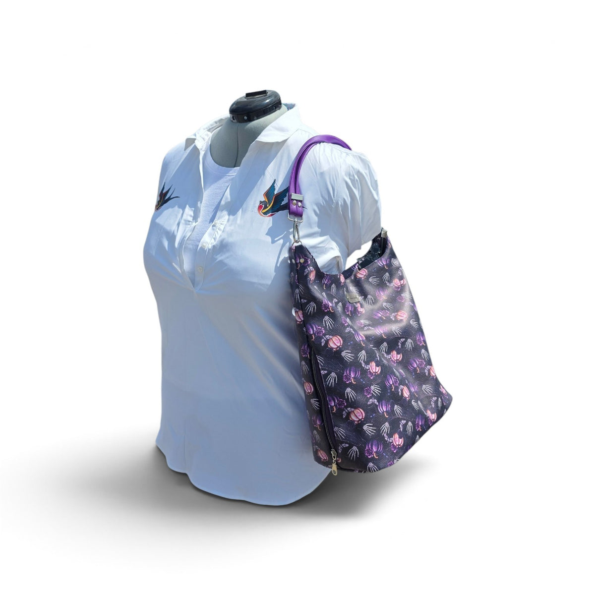 A black tote bag with a pink and purple pattern and a purple shoulder strap, displayed on a white mannequin torso wearing a white shirt against a white background.