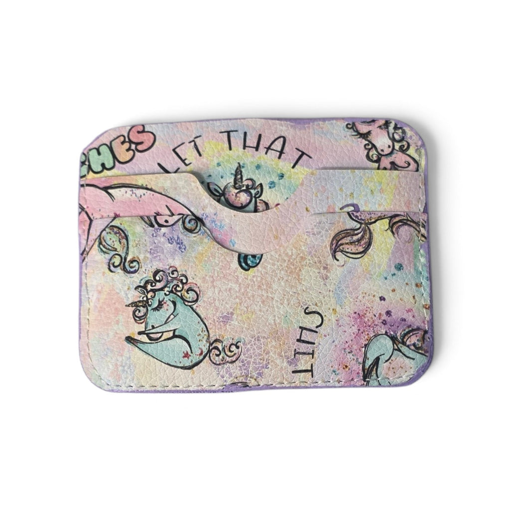 A small rectangular card holder or wallet with rounded corners, featuring a pastel multicolor watercolor-style print with cartoon unicorn illustrations and text including 'LET THAT' and 'STFU'.