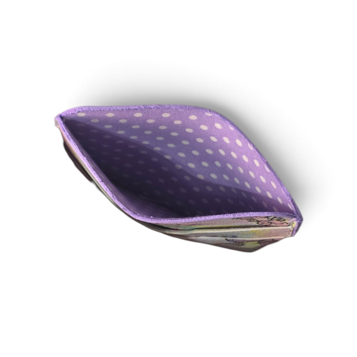 A small  card holder shown open from above on a white background. The interior is lavender purple with white polka dots, and a small portion of the exterior pattern is visible along the lower edge.