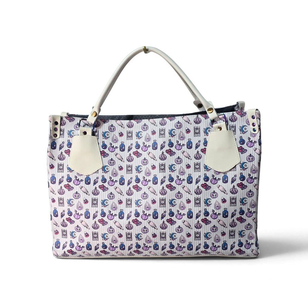A structured tote bag with a white base covered in a repeating pattern of small purple and blue illustrated motifs. It features light gray top handles, off-white leather-like hanging tags, and a dark navy zipper closure at the top.