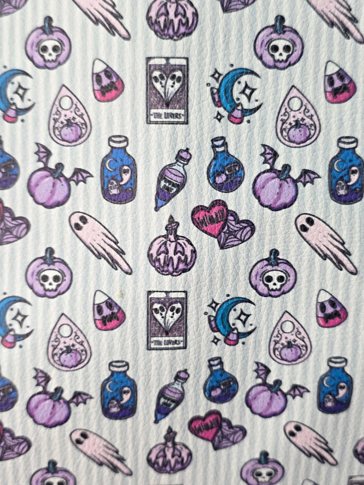 A close-up of a white textured fabric featuring a repeating pattern of whimsical, hand-drawn Halloween-themed illustrations in purple, pink, and blue, including pumpkins, skulls, ghosts, and tarot cards.