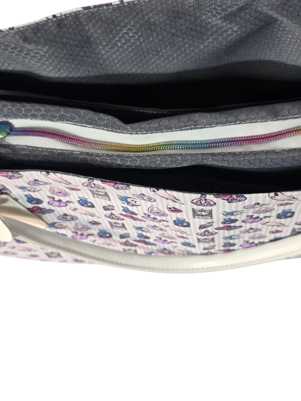Close-up of a handbag's interior showing a gray honeycomb-patterned lining, a rainbow-colored zipper, and a white fabric panel printed with small colorful cartoon motifs.