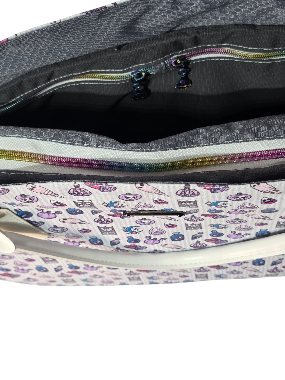 Close-up of a patterned zippered pouch or bag interior, showing a white exterior with a multicolor print of desserts and coffee cups, a gray patterned lining, and a rainbow-colored zipper.