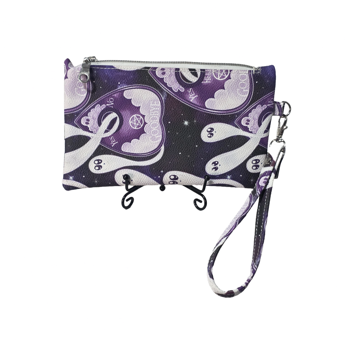 A wristlet clutch bag with a purple and white cartoon ghost pattern on a dark background, featuring a wrist strap and silver zipper closure, displayed on a black stand against a white background.