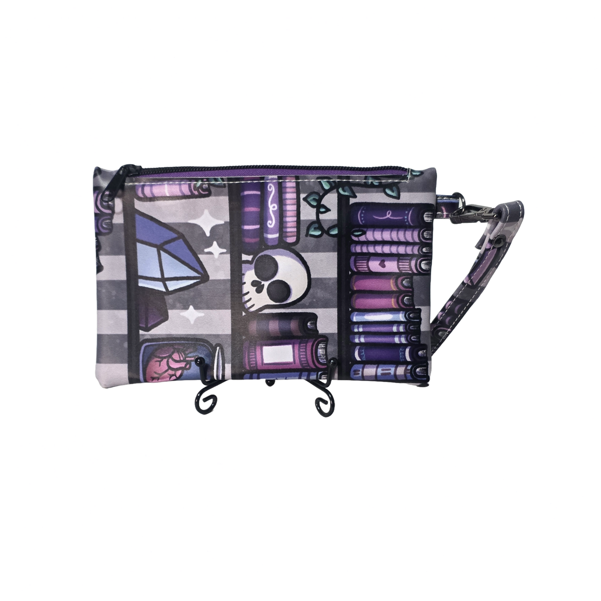 A wristlet pouch with a gothic occult-themed print featuring purple books, a skull, crystals, and a brain on a gray and white striped background, complete with a matching wrist strap.