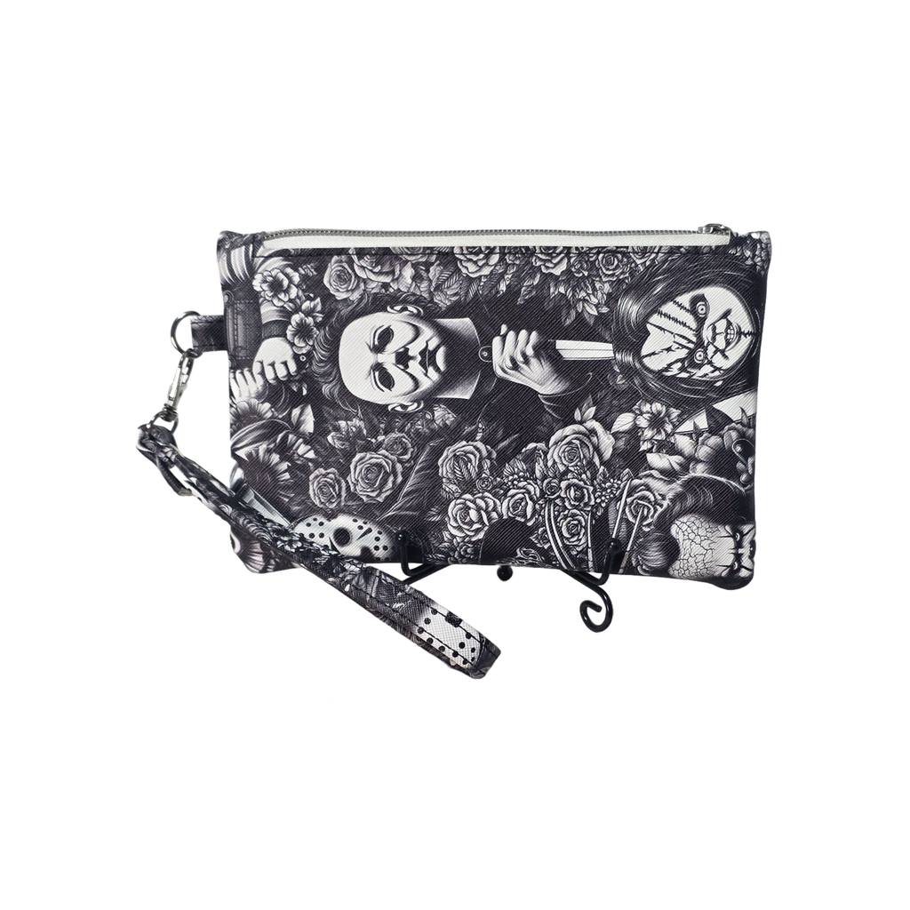 A black and white gothic-themed wristlet clutch featuring a detailed print of Pennywise the Clown, roses, and skulls, complete with a matching wrist strap and metal zipper closure.
