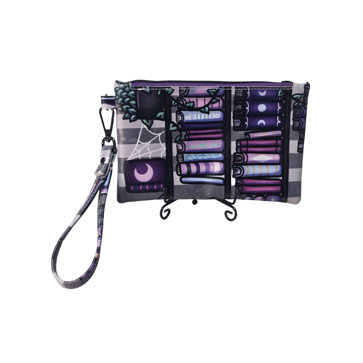A Halloween-themed wristlet clutch with a matching wrist strap, featuring a spooky bookshelf design filled with purple and black books, a spiderweb motif, and moon phases on a white background.