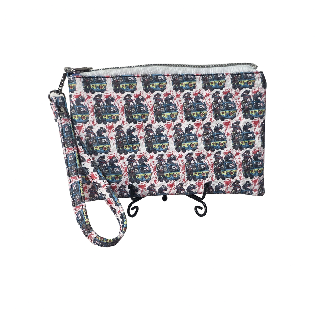 A wristlet clutch bag with a repeating pattern of vintage steam locomotives in blue, red, yellow, and green on a white background. The bag has a top zipper closure and a matching printed wrist strap, displayed on a small black stand against a plain white background.