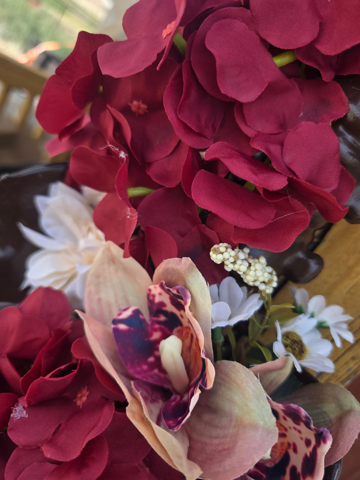 A close-up of a floral arrangement featuring deep burgundy hydrangeas, a beige and purple orchid, and small white daisy-like flowers.