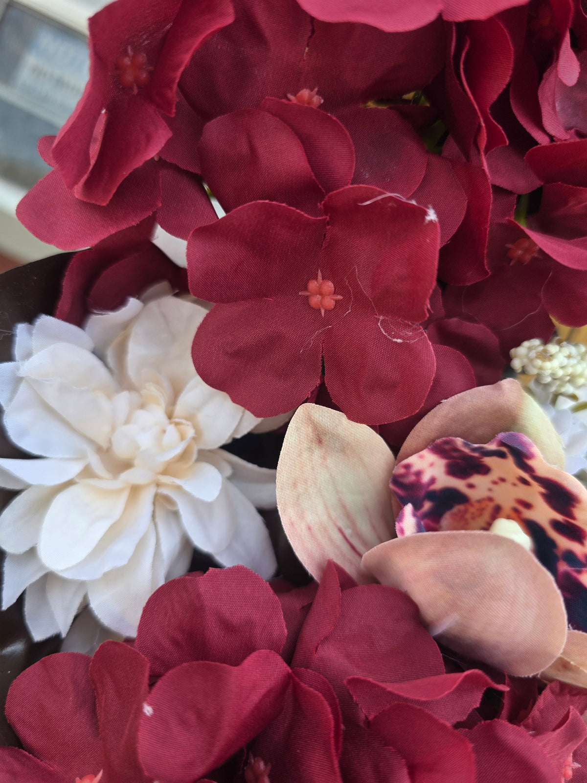A close-up of artificial flowers, dominated by deep burgundy hydrangea blooms, a large white flower on the left, and a leopard-print orchid on the right.