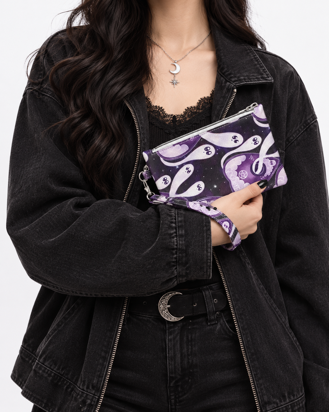 A person wearing a black denim jacket and black lace top holds a purple and white ghost-pattern clutch bag.