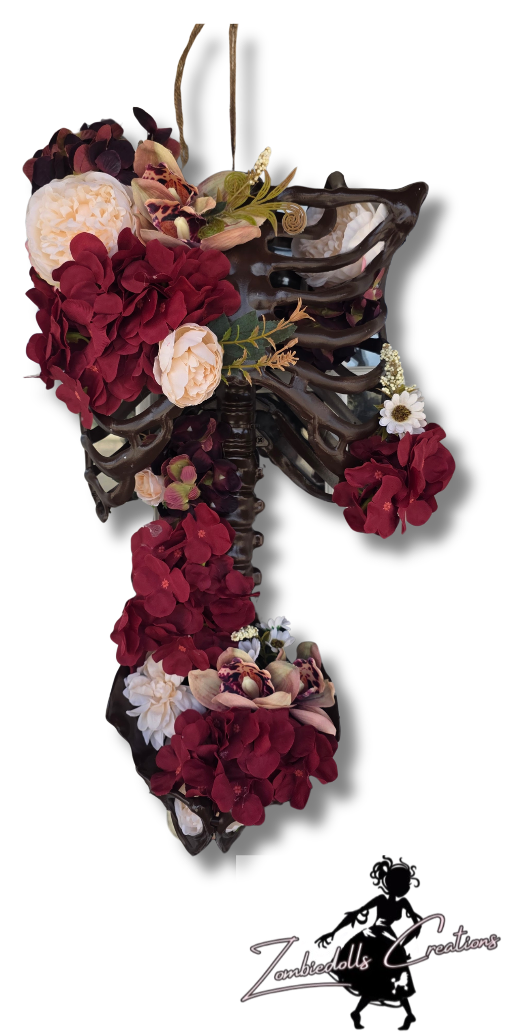 A gothic-style hanging cross made from a dark brown rib cage, adorned with deep burgundy and cream faux flowers, green leaves, and small white daisies, shown against a white background with a 'Zephyrus Creations' logo in the bottom right corner.